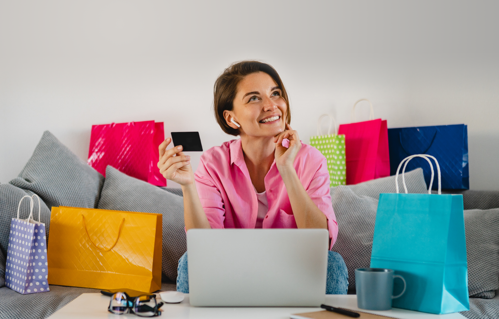 Woman in pink shirt with shopping bags and laptop, holding a credit card.