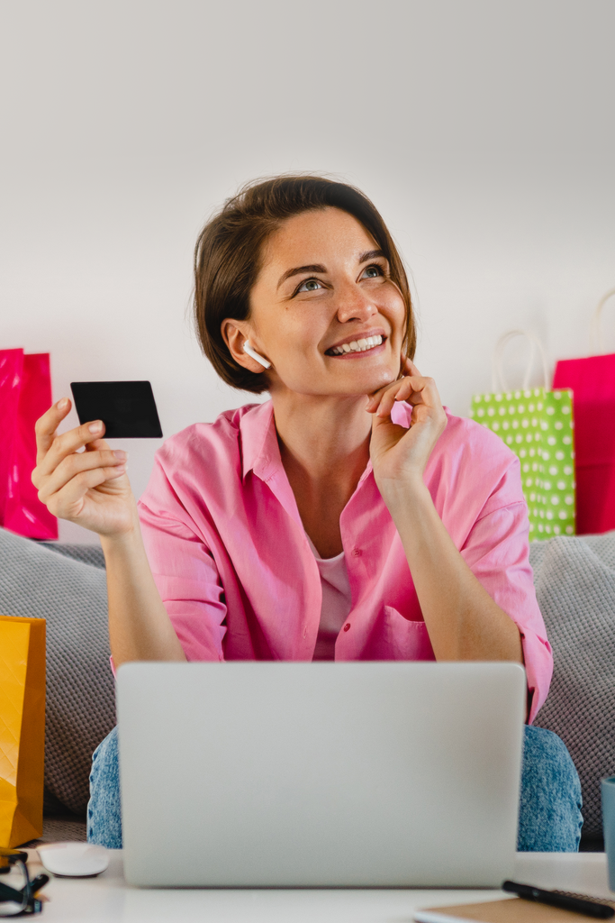 Woman in pink shirt with shopping bags and laptop, holding a credit card.